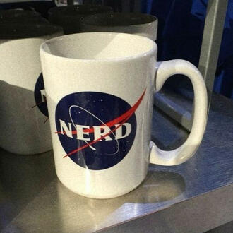 A photo of a white mug with a NASA logo on it sitting on a table. The text of the NASA logo has been edited to read "NERD" instead.
