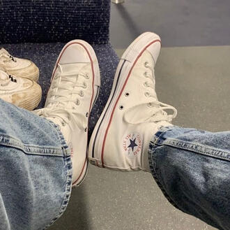 a photo of someone wearing jeans and white converse resting their legs on a bus seat.